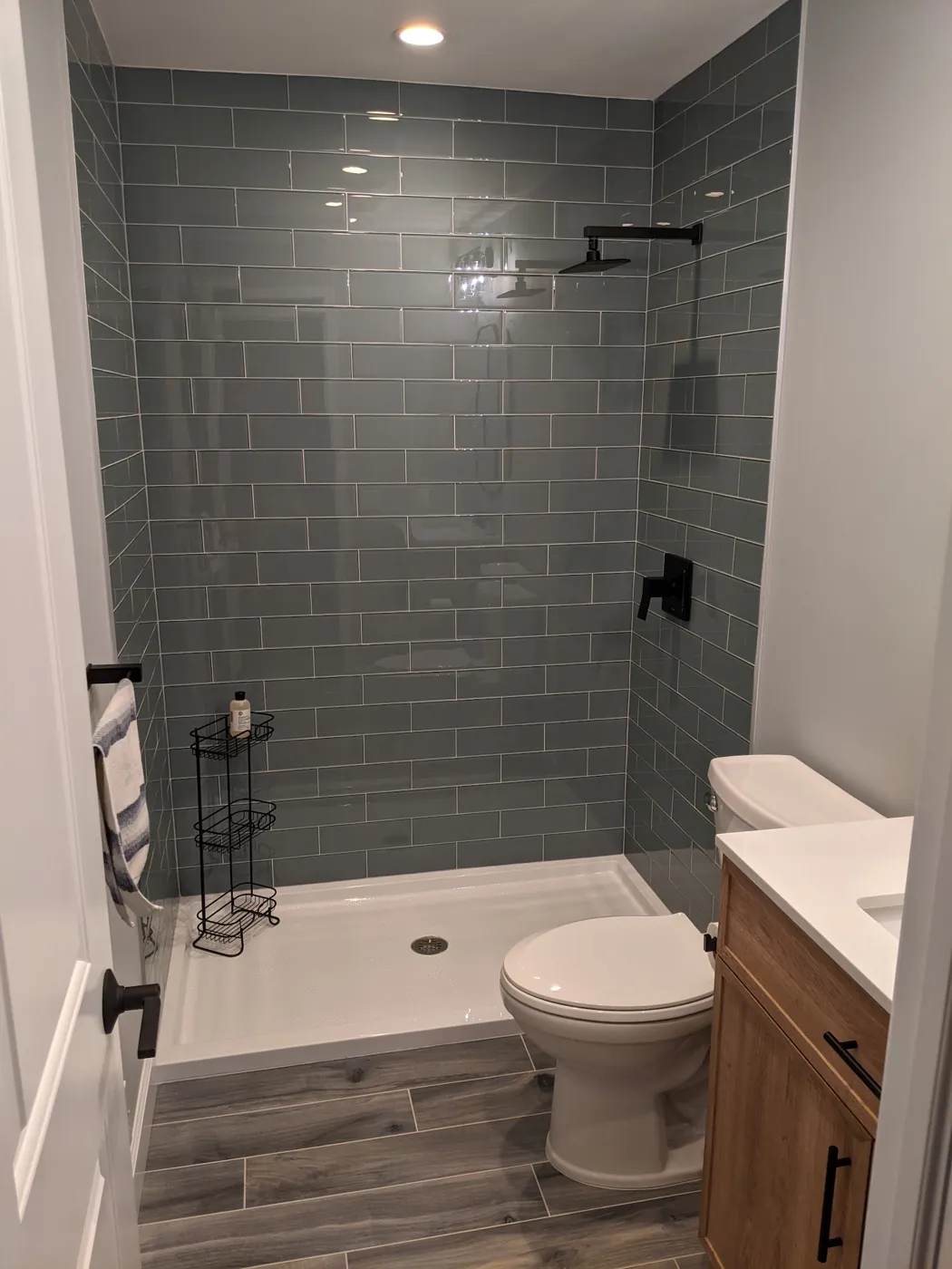 Tub-to-shower conversion with grey glass subway tile, matte black fixtures, and wood-look porcelain plank floor in Monmouth County, NJ