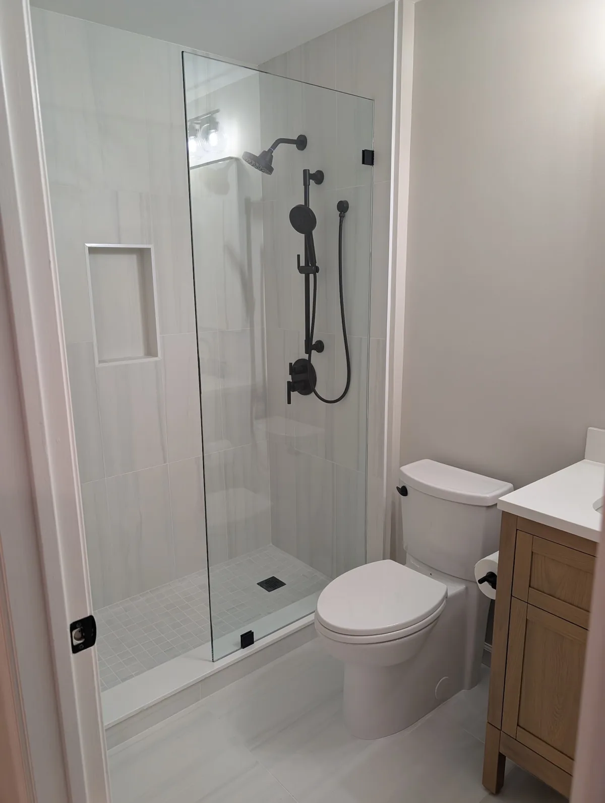 Hall bathroom remodel in Monmouth County, NJ: walk-in shower with frameless glass, matte black fixtures, tiled niche, and a white oak vanity by RSC Contracting