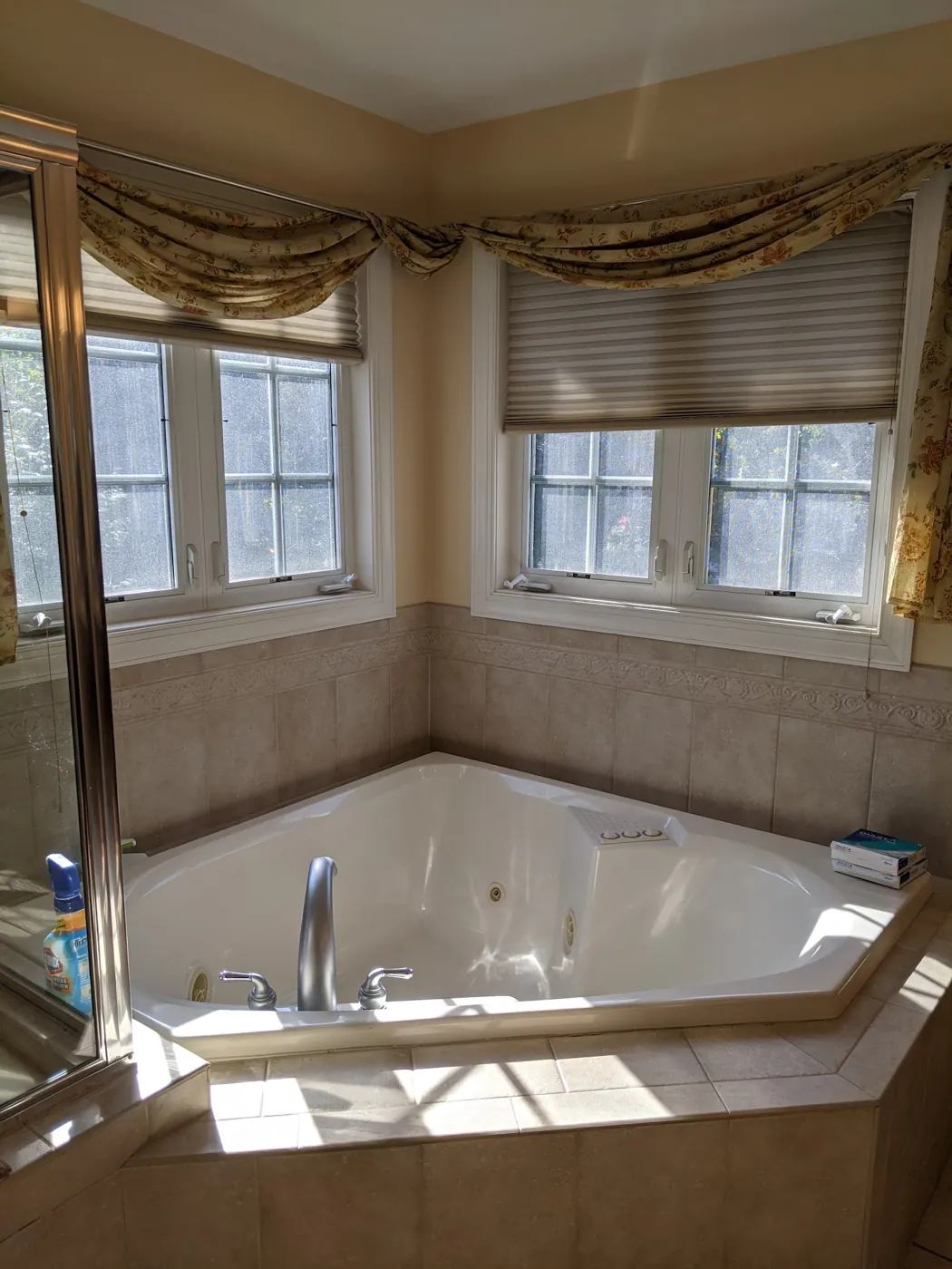 Before: 1990s primary bathroom with a corner jetted tub on a tiled platform under bay windows