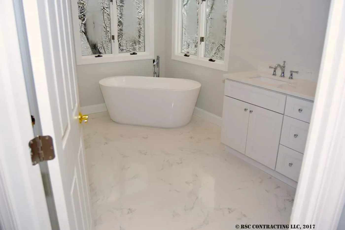 After: the same corner with a freestanding soaking tub, floor-mounted filler, and marble-look porcelain floor