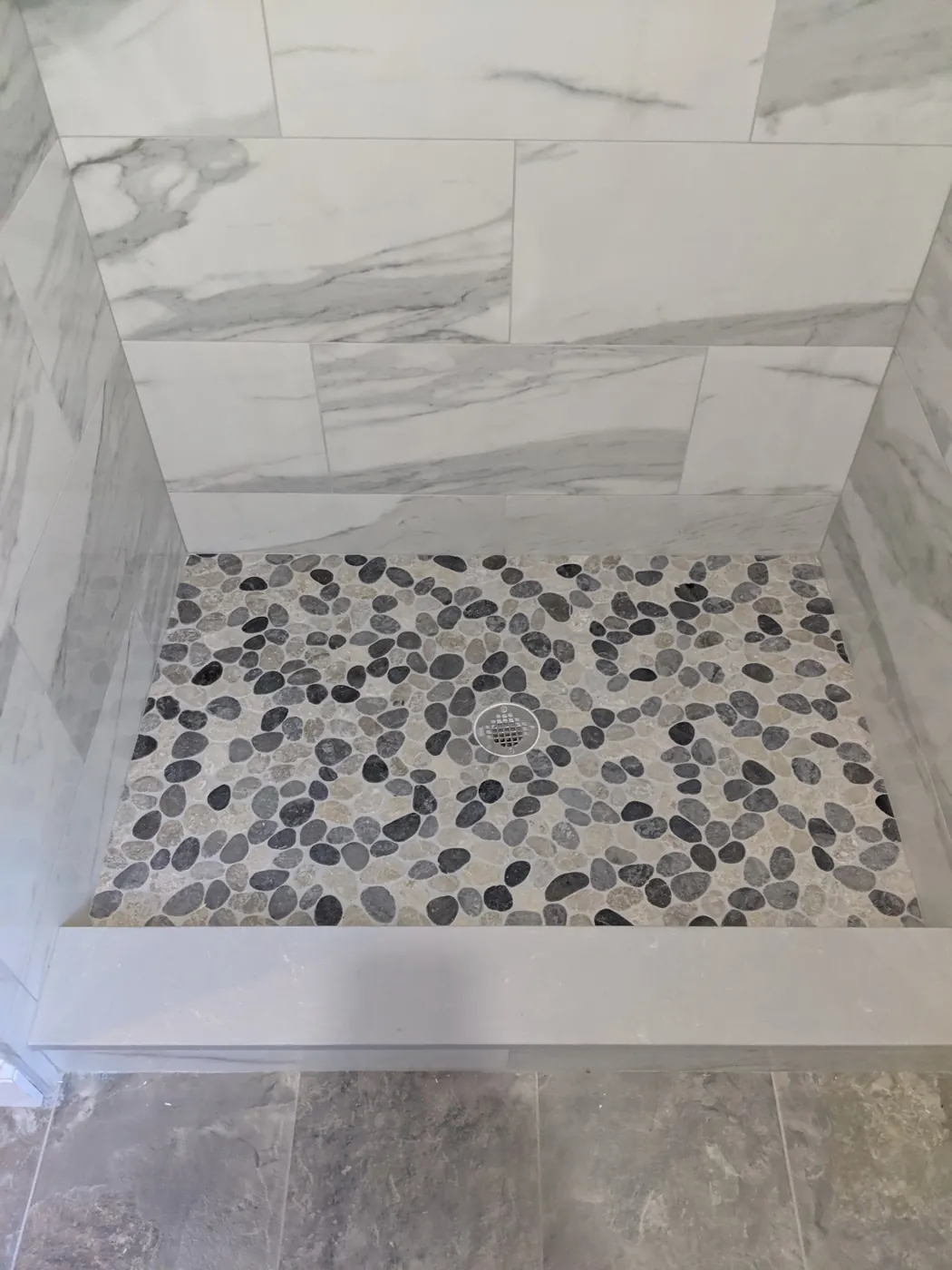 Walk-in shower with large-format marble-look porcelain tile and a river pebble floor in a Monmouth County, NJ bathroom remodel