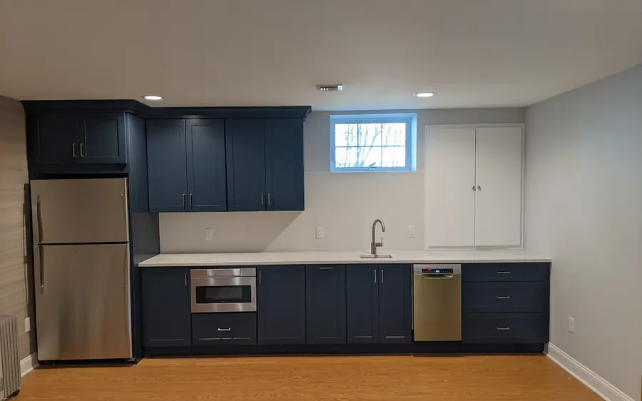 Finished basement in Monmouth County, NJ with a navy kitchenette, quartz counter, and recessed lighting