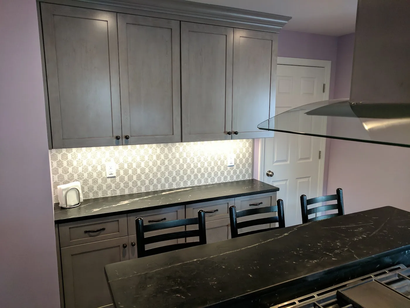 Soapstone-look counters with a raised island seating ledge and hex tile backsplash in a grey kitchen