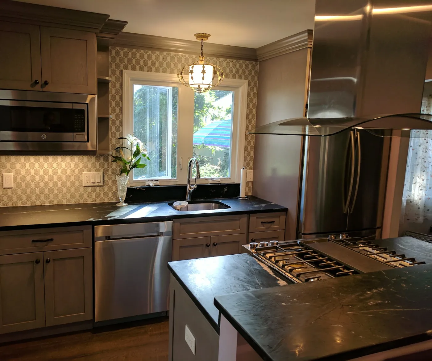 Grey stained kitchen cabinets with dark soapstone-look counters, an island cooktop with glass hood, and a hex tile backsplash in a Monmouth County, NJ kitchen remodel