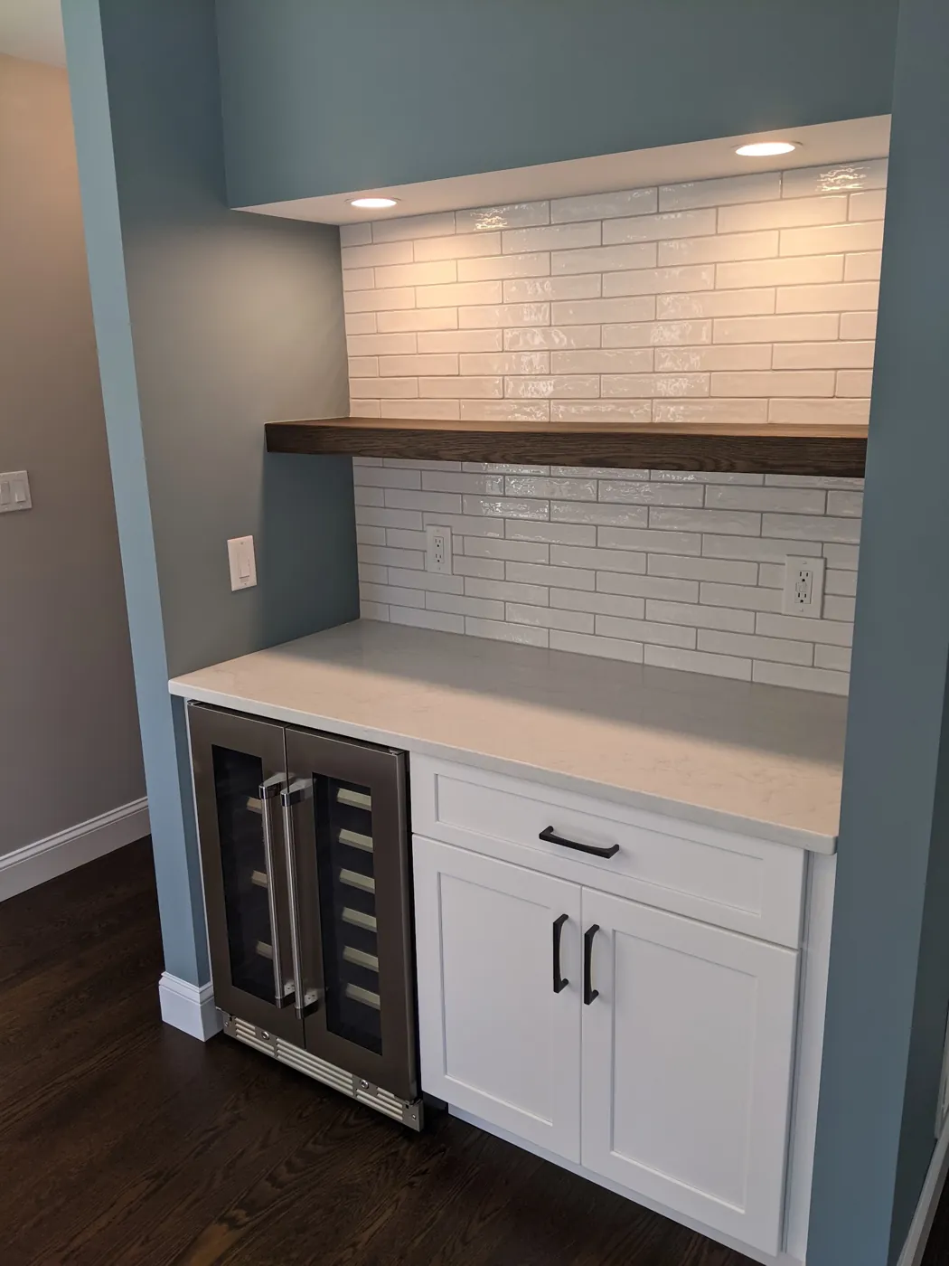 Built-in beverage bar with a wine fridge, quartz counter, floating walnut shelf, and glossy subway tile