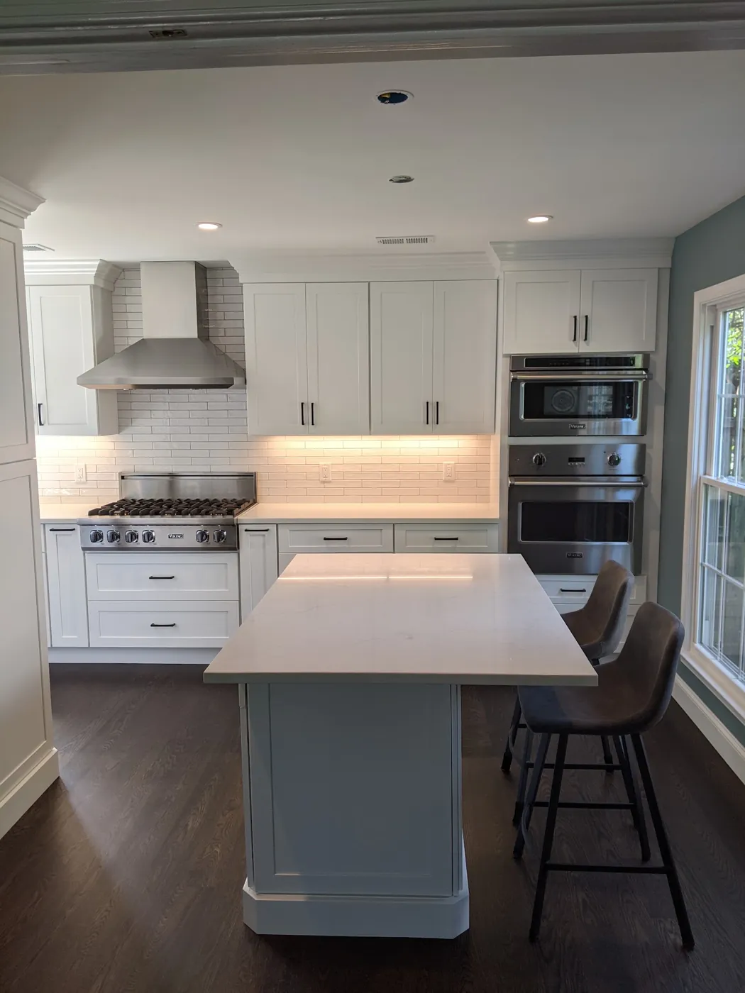 White shaker kitchen with a quartz island, stainless chimney hood, wall ovens, and blue-grey walls in Monmouth County, NJ