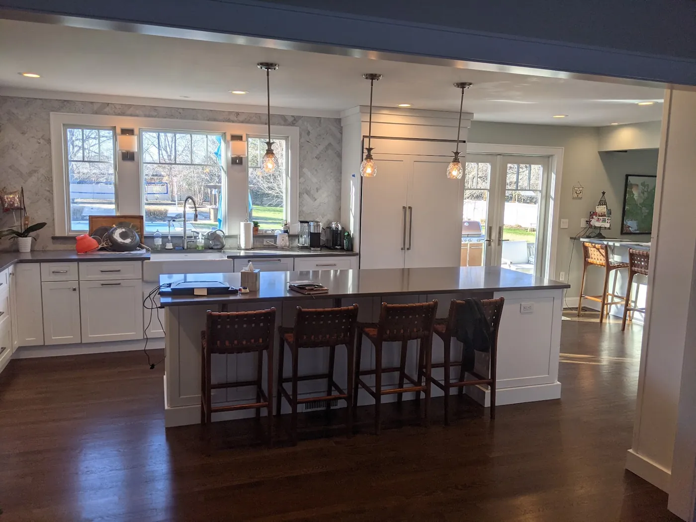 Kitchen remodel in Monmouth County, NJ with white shaker cabinets, a large seated island, a stained wood range hood, and marble herringbone backsplash by RSC Contracting